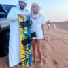 safari guide with a tourist carrying a sand board over desert safari tour